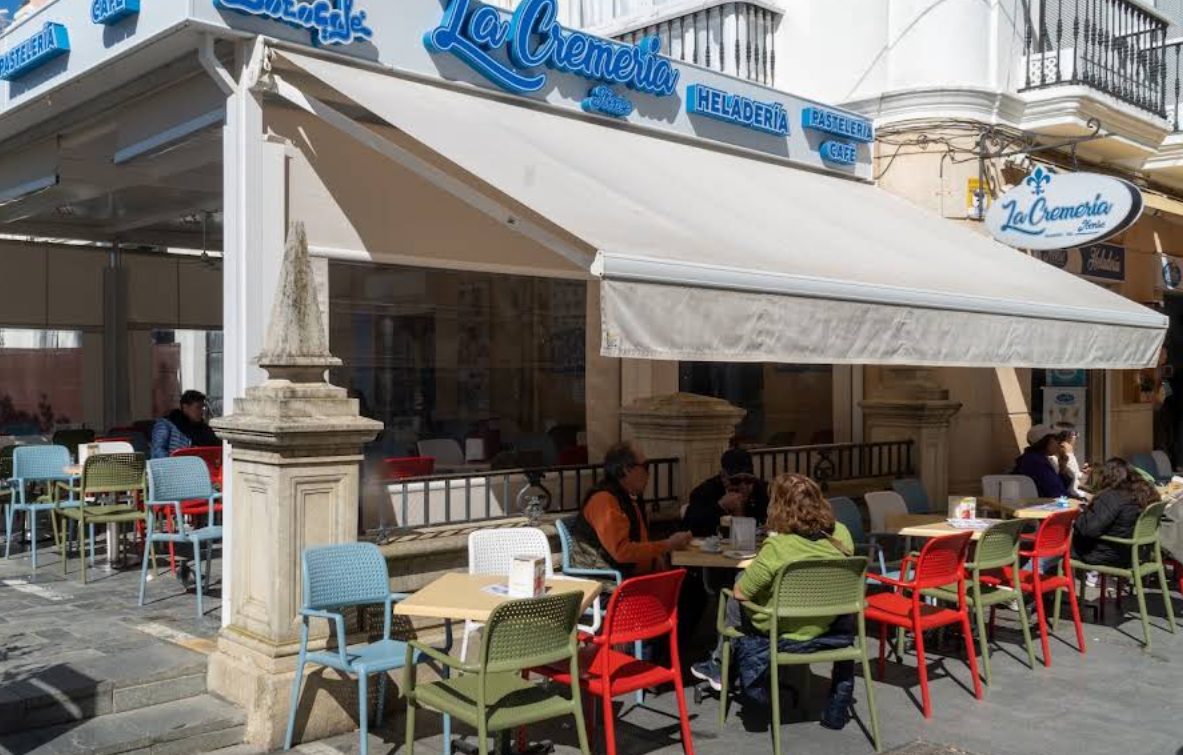 Terraza de La Cremería Ibense con sillas rojas, azules y verdes bajo el toldo